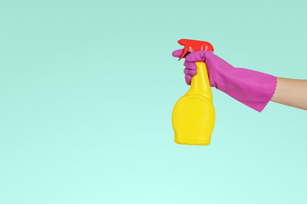 Image of a hand wearing a rubber glove and holding a spray bottle.