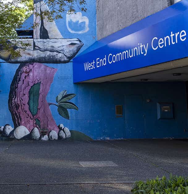 Exterior view of the West End Community Centre in Vancouver, featuring blue awnings, a mural with nature artwork, and the Joe Fortes Library branch entrance